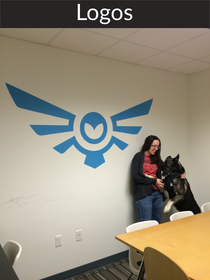A girl stands in front of an office logo wall mural. Botsy transferred the office logo to a wall. The drawing machine scales up and speeds up the office mural painting process without a projector, graphite transfer paper or punched one.